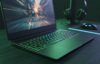 Budżetowy laptop gamingowy z RTX 5060. Podświetlana klawiatura RGB świeci na zielono i niebiesko na ciemnym biurku. Dynamiczna gra akcji widoczna na ekranie.