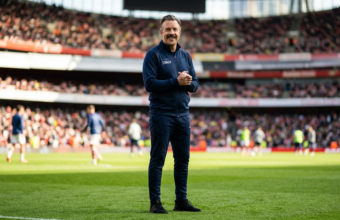 Uśmiechnięty Ted Lasso z wąsami w granatowym dresie na boisku. Trener z 4 sezonu serialu Apple TV+ na tle stadionu. Premiera nowych odcinków i informacje.