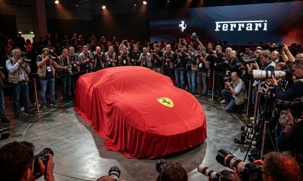 Premiera Ferrari Luce. Nowy model Ferrari pod płachtą z logo, otoczony przez fotoreporterów. Oczekiwanie na odsłonięcie sportowego auta, którego kształt jest ukryty.