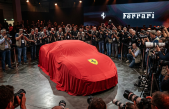 Premiera Ferrari Luce. Nowy model Ferrari pod płachtą z logo, otoczony przez fotoreporterów. Oczekiwanie na odsłonięcie sportowego auta, którego kształt jest ukryty.