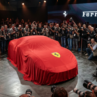 Premiera Ferrari Luce. Nowy model Ferrari pod płachtą z logo, otoczony przez fotoreporterów. Oczekiwanie na odsłonięcie sportowego auta, którego kształt jest ukryty.