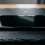 Elegancki polski smartfon bez usług Google na ciemnym kamieniu. Wyłączony bezramkowy ekran i metaliczna obudowa podkreślają nowoczesny design urządzenia.