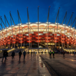 Podświetlony Stadion Narodowy w Warszawie, Polska. Biało-czerwona elewacja o zmierzchu. Orlen inwestuje w prawa do nazwy tej prestiżowej areny biznesowej.