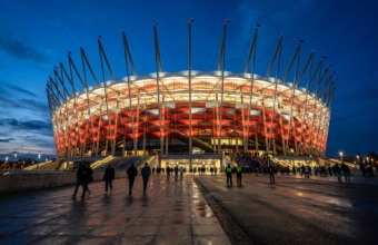 Podświetlony Stadion Narodowy w Warszawie, Polska. Biało-czerwona elewacja o zmierzchu. Orlen inwestuje w prawa do nazwy tej prestiżowej areny biznesowej.