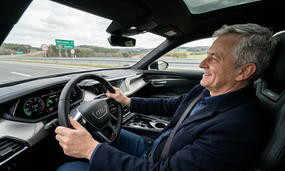 Uśmiechnięty 57-letni Polak kieruje elektrycznym Audi na pustej drodze szybkiego ruchu. Polska i świat: zadowolony kierowca wygodnie oparty plecami o fotel.