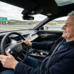 Uśmiechnięty 57-letni Polak kieruje elektrycznym Audi na pustej drodze szybkiego ruchu. Polska i świat: zadowolony kierowca wygodnie oparty plecami o fotel.