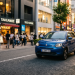 Tani elektryk Suzuki e-Sky mknie przez nowoczesną dzielnicę w Polsce i na świecie. Lśniące auto elektryczne odbija światła miasta podczas złotej godziny.