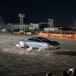 Nowa srebrna futurystyczna Tesla Roadster z silnikami SpaceX unosi się nocą dzięki wywietrznikom w podwoziu i bokach. Widzowie w oddali na torze SpaceX.