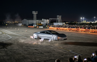 Nowa srebrna futurystyczna Tesla Roadster z silnikami SpaceX unosi się nocą dzięki wywietrznikom w podwoziu i bokach. Widzowie w oddali na torze SpaceX.
