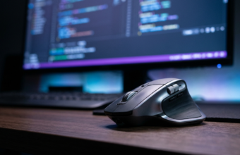 Ergonomiczna mysz Logitech MX Master 4 na ciemnym biurku, w tle kod na ekranie. Komputery, AI i oprogramowanie dla programistów, Polska i świat.